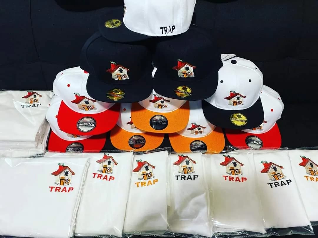 Assorted caps and white garments embroidered with a TRAP house logo