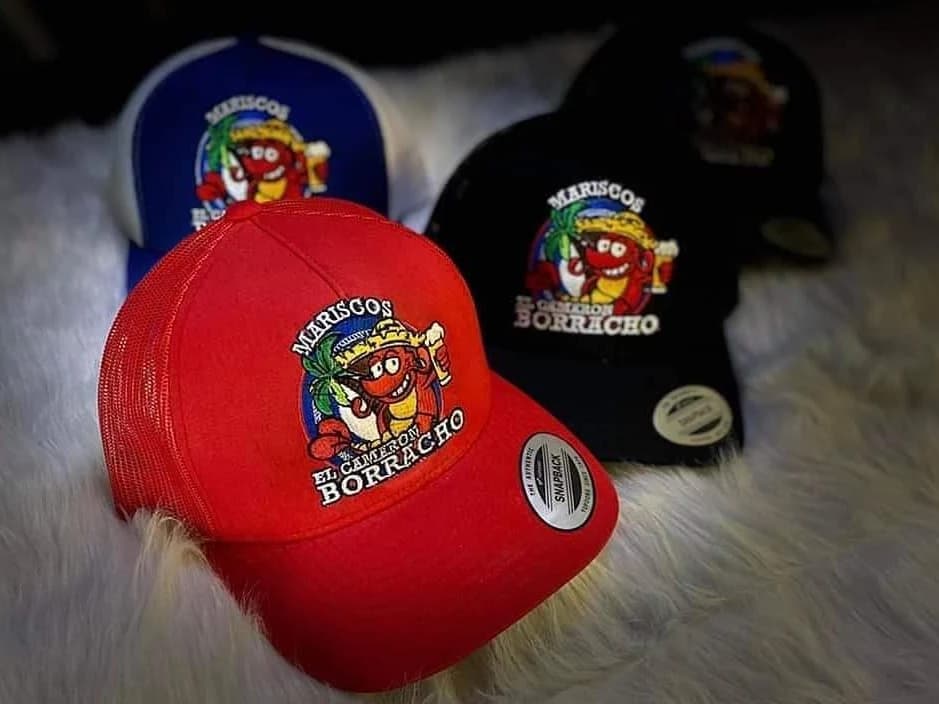 Red, black and blue caps embroidered with a Mariscos shrimp logo